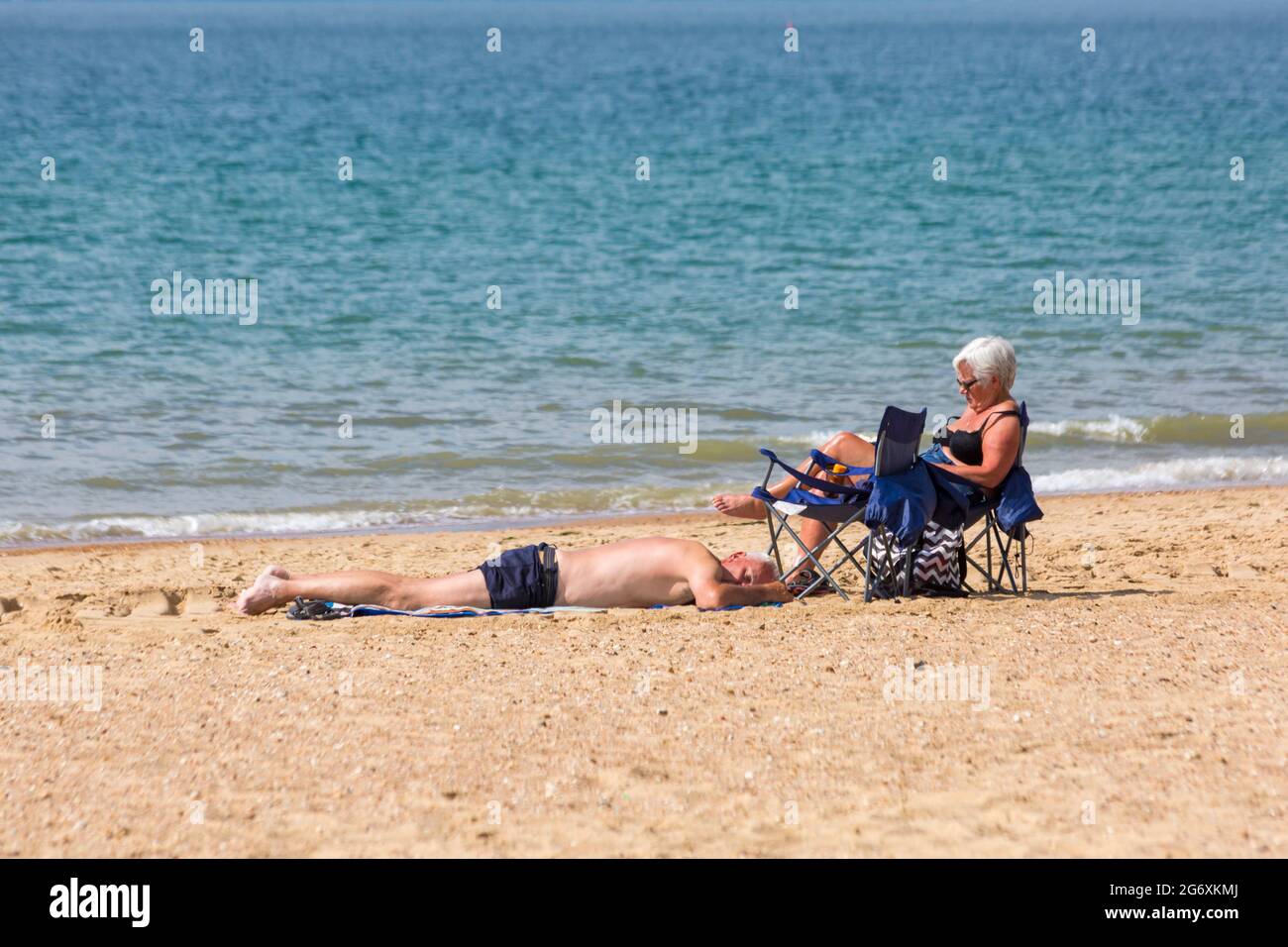 Bournemouth, Dorset, Royaume-Uni. 9 juillet 2021. Temps au Royaume-Uni : belle journée ensoleillée, mais humide sur les plages de Bournemouth, tandis que les amateurs de soleil se dirigent vers le bord de mer pour profiter du soleil. Couple sur la mer, homme allongé sur le sable, bain de soleil, femme assise reposant sur le siège. Crédit : Carolyn Jenkins/Alay Live News Banque D'Images