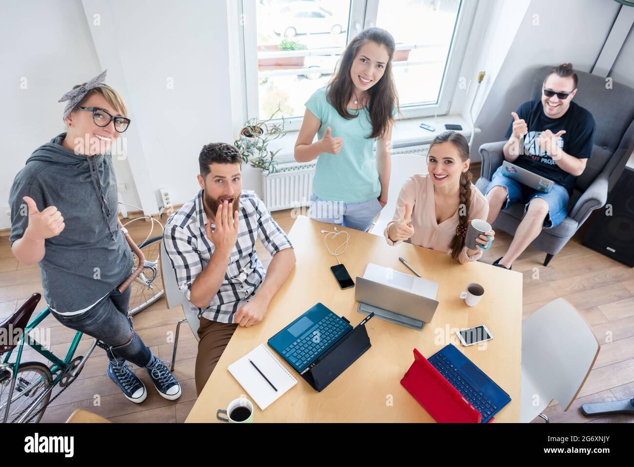 Vue en grand angle d'un groupe de jeunes gens joyeux montrant les pouces comme un signe de bonheur, pour travailler en commun dans un espace de bureau moderne partagé Banque D'Images