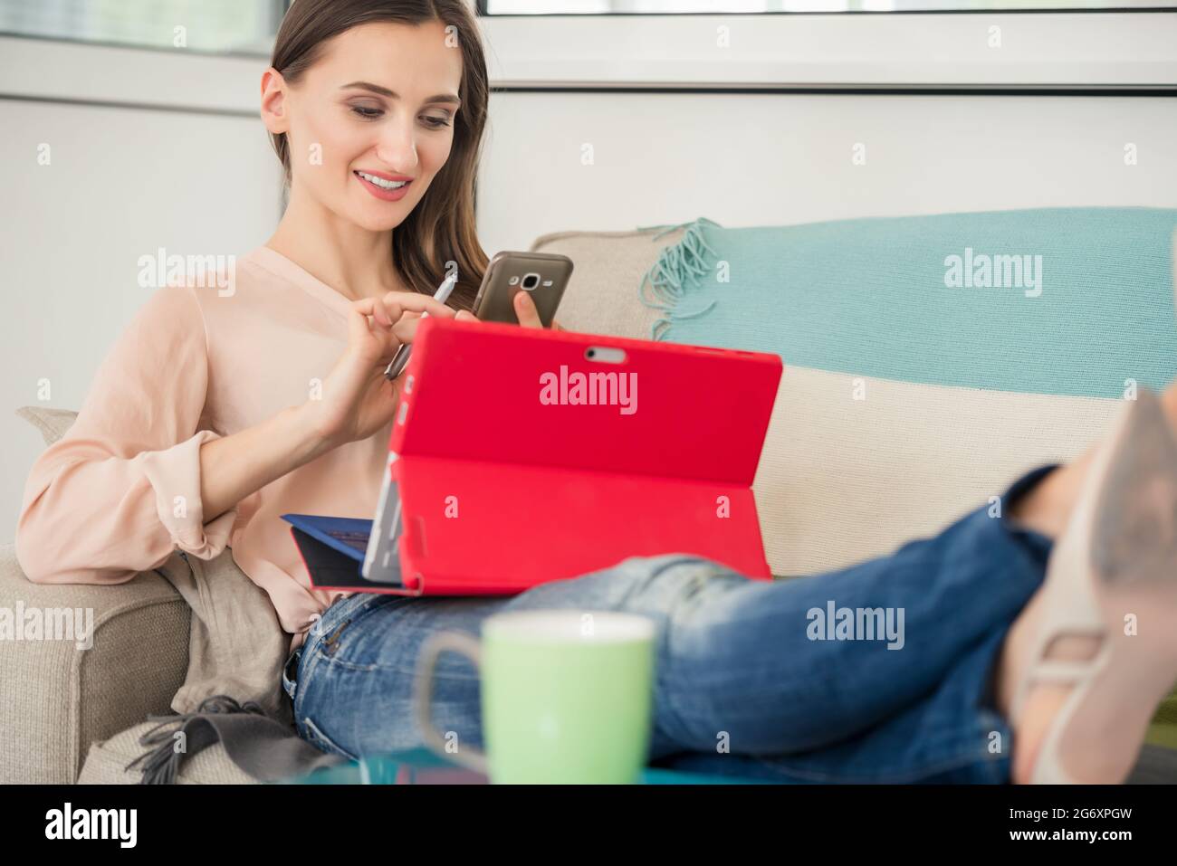 Longueur pleine vue latérale d'une jeune femme créative assise sur un canapé avec ses pieds sur une table à café, tout en travaillant sur le comprimé dans le bureau d'un c Banque D'Images