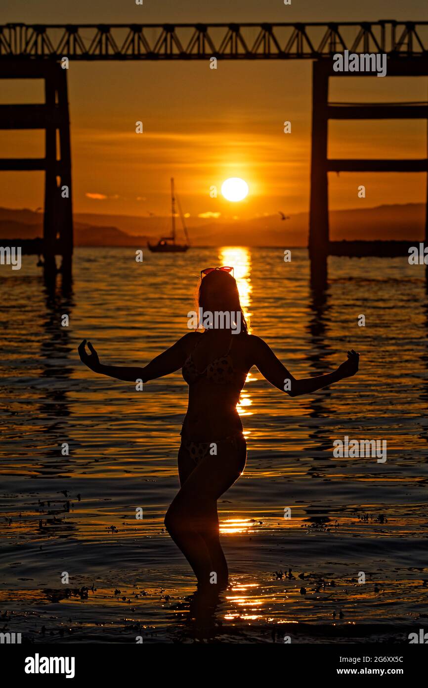 Photo : Natasha Jenkins dans la mer au lever du soleil, vue à travers la station de bateau RNLI à Mumbles, près de Swansea, pays de Galles, Royaume-Uni. Dimanche 13 juin 2021 objet : Banque D'Images