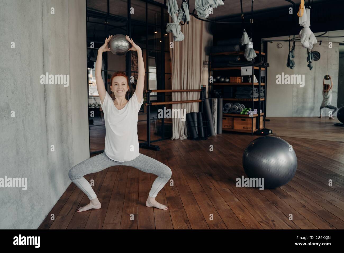 Bonne sportive femelle en usure active tenant le mini-fitball au-dessus de la tête en position semi-assise Banque D'Images