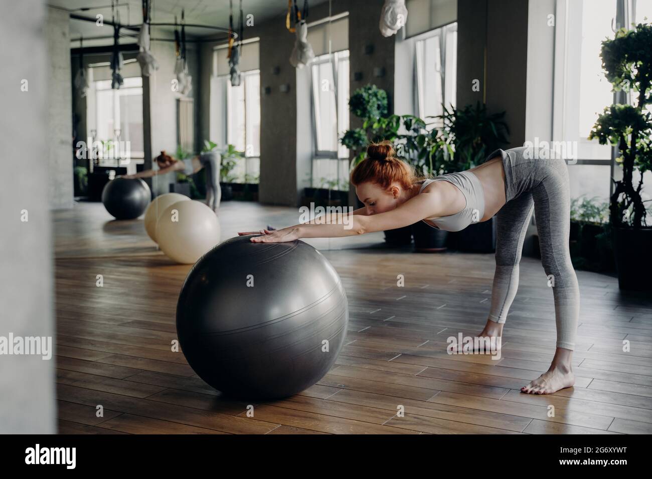 Femme mince qui s'étire avec un ballon d'exercice tout en s'entraîner dans un studio de fitness moderne Banque D'Images