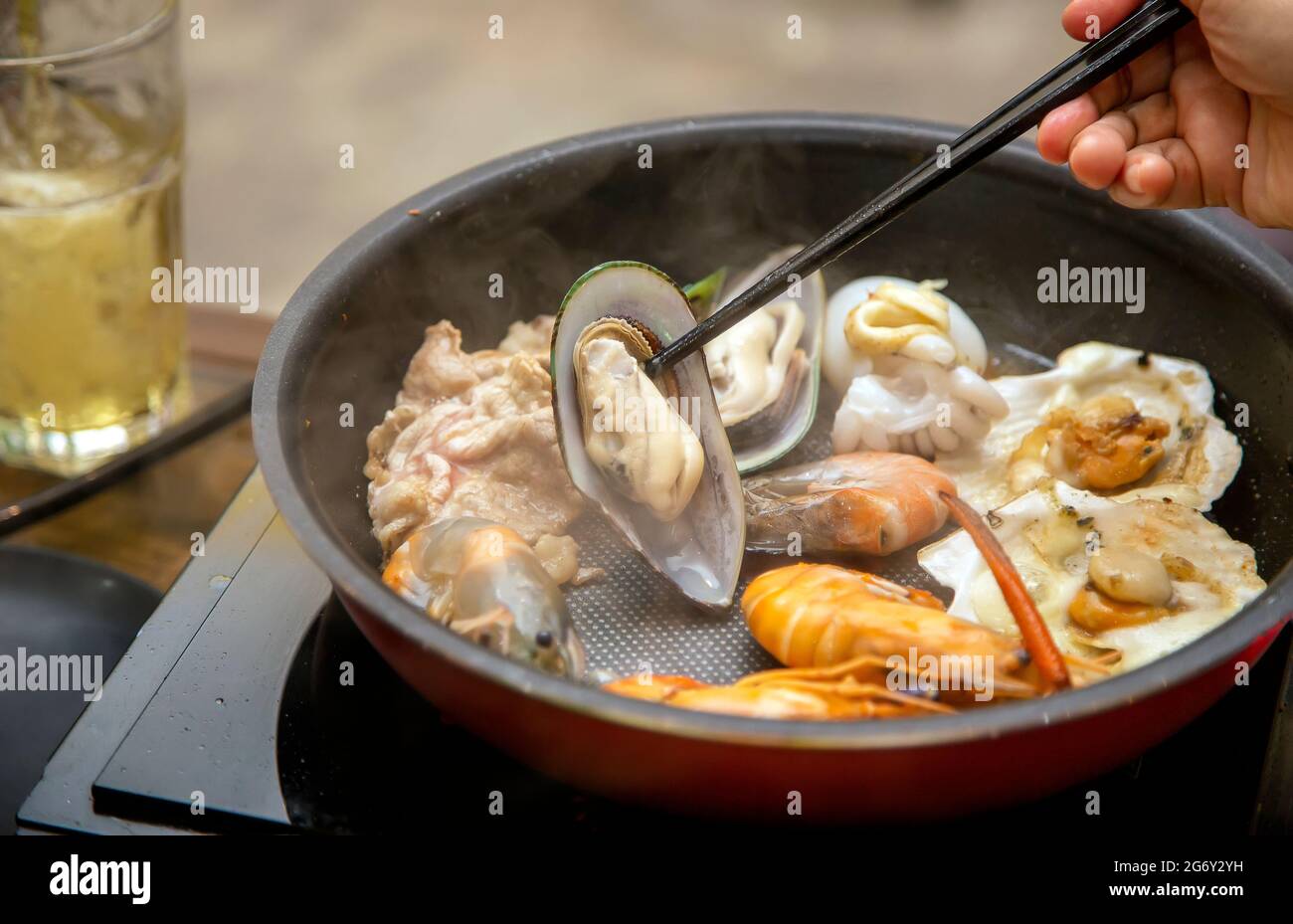 faire cuire des huîtres et des fruits de mer manu avec une poêle chaude électrique et conserver avec un bâton de hache sur la table du dîner Banque D'Images