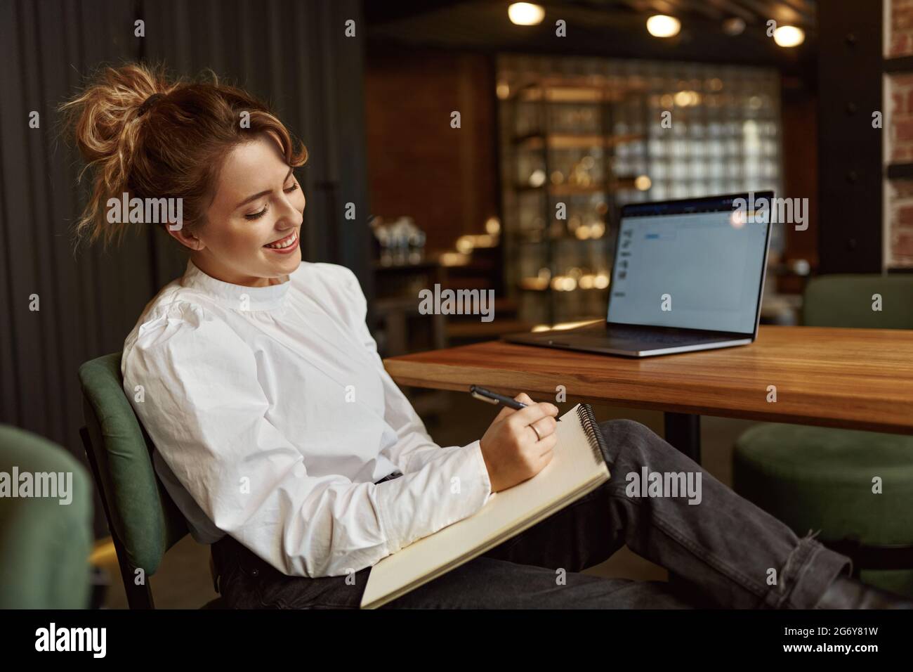 Femme souriante prenant des notes tout en travaillant sur un ordinateur portable Banque D'Images