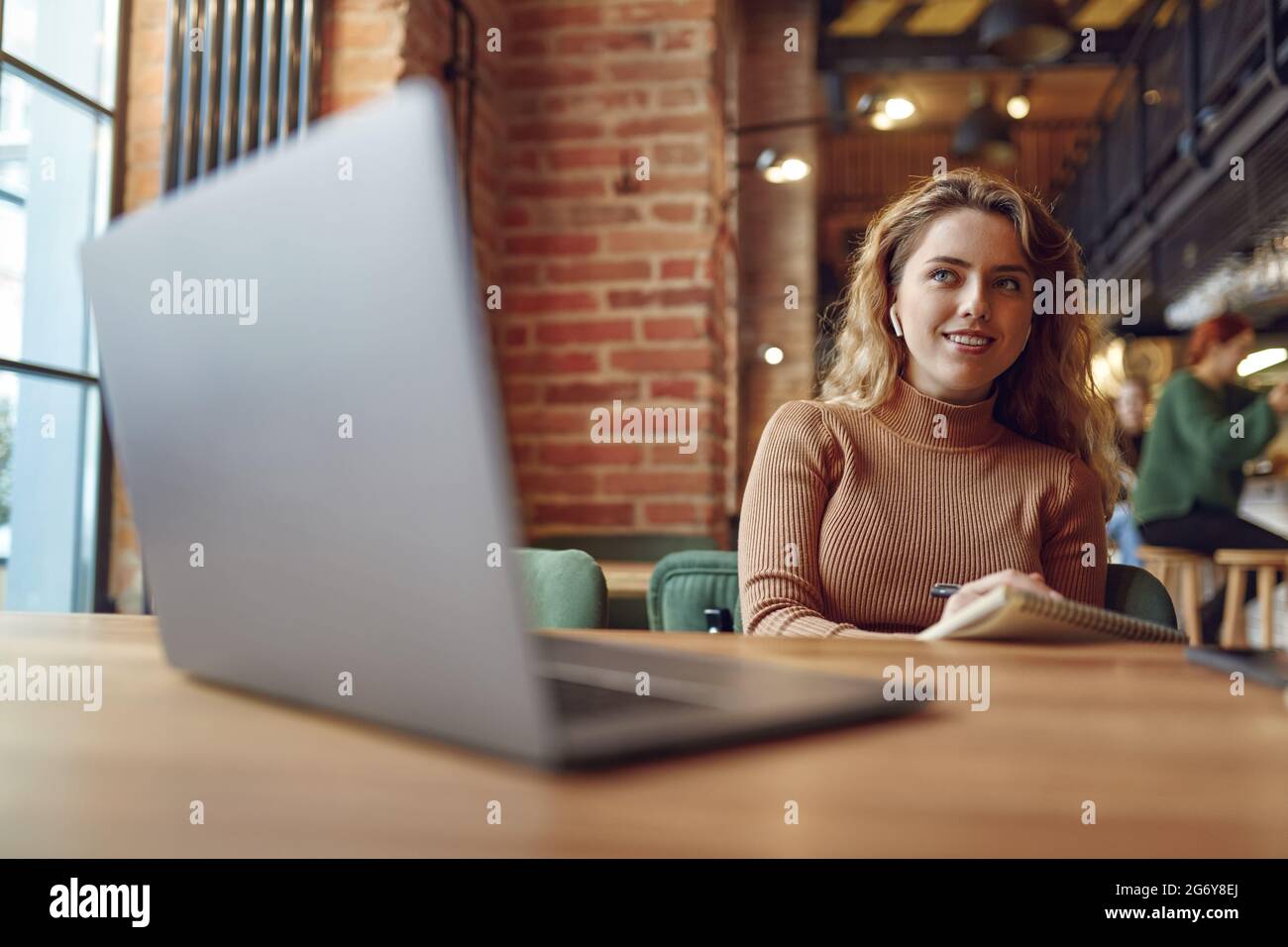 Femme utilisant des écouteurs et un ordinateur portable pour étudier au café Banque D'Images