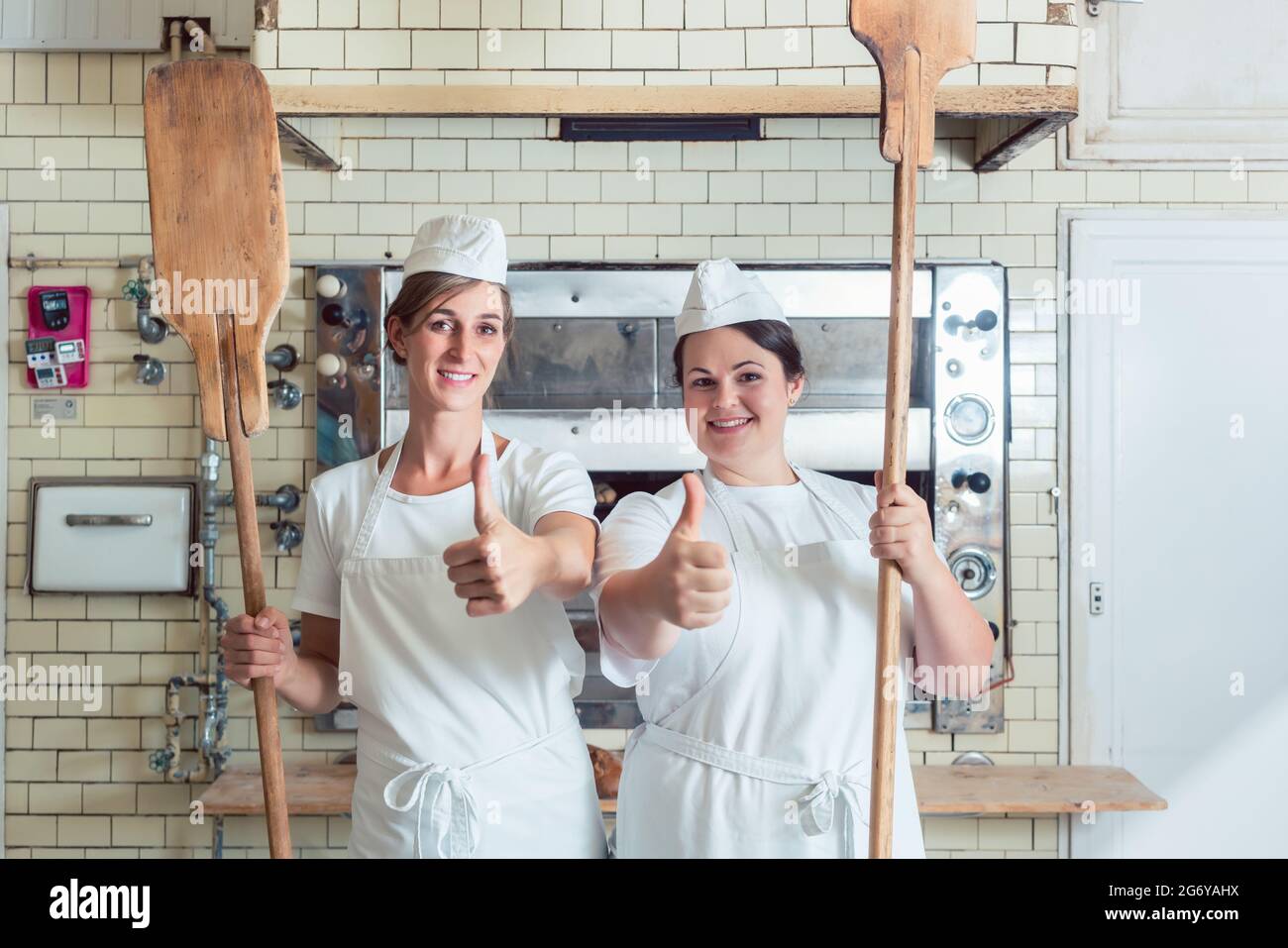 Une équipe de boulangeuses se tenant fièrement dans la boulangerie, se portant les pouces Banque D'Images