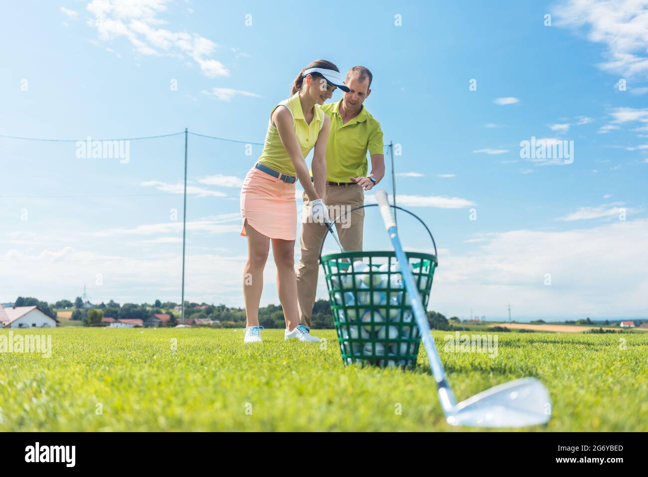 Pleine longueur d'une jeune femme gaie apprenant la bonne prise et de se déplacer pour utiliser le club de golf de fer, sous la direction d'un enseignant de sexe masculin ou Banque D'Images