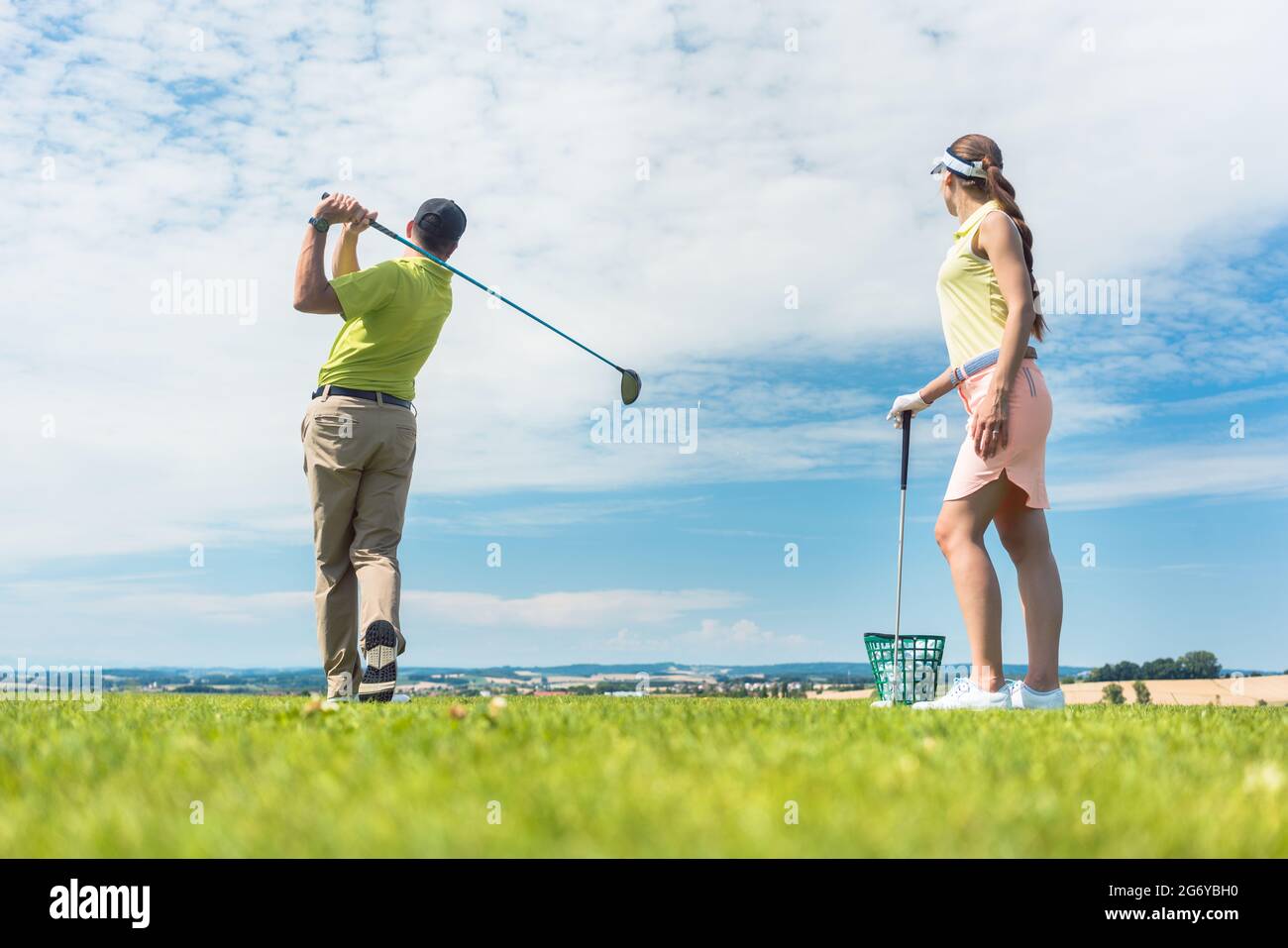 Full Length of a young woman smiling tout en pratiquant la bonne décision pour la frappe au cours de golf avec un professionnel qualifié de la classe player outdoors Banque D'Images