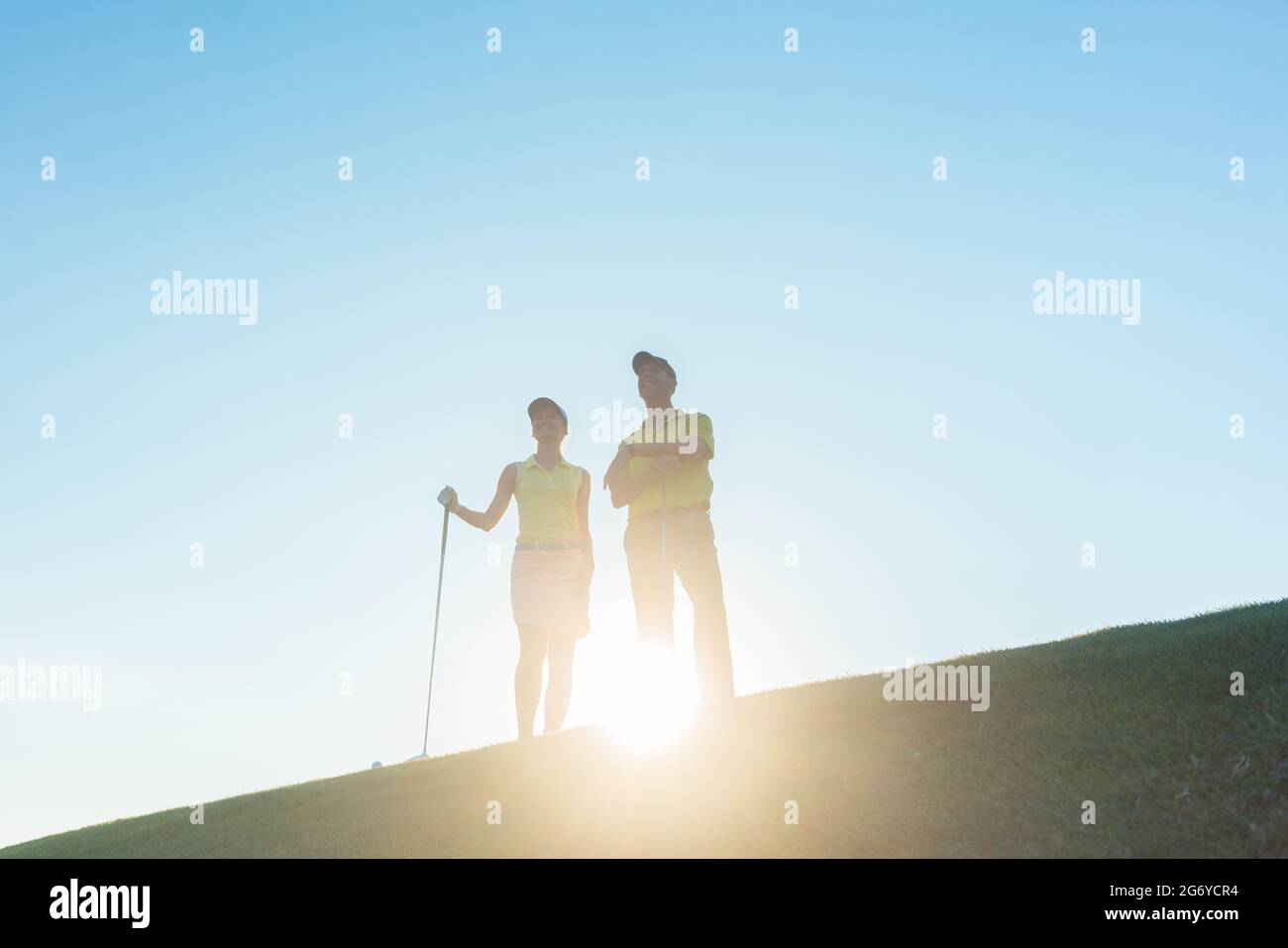 Vue en contre-angle de la silhouette d'un homme pointant vers l'horizon tout en se tenant à côté de sa partenaire femelle, sur un parcours de golf professionnel contre le soleil Banque D'Images