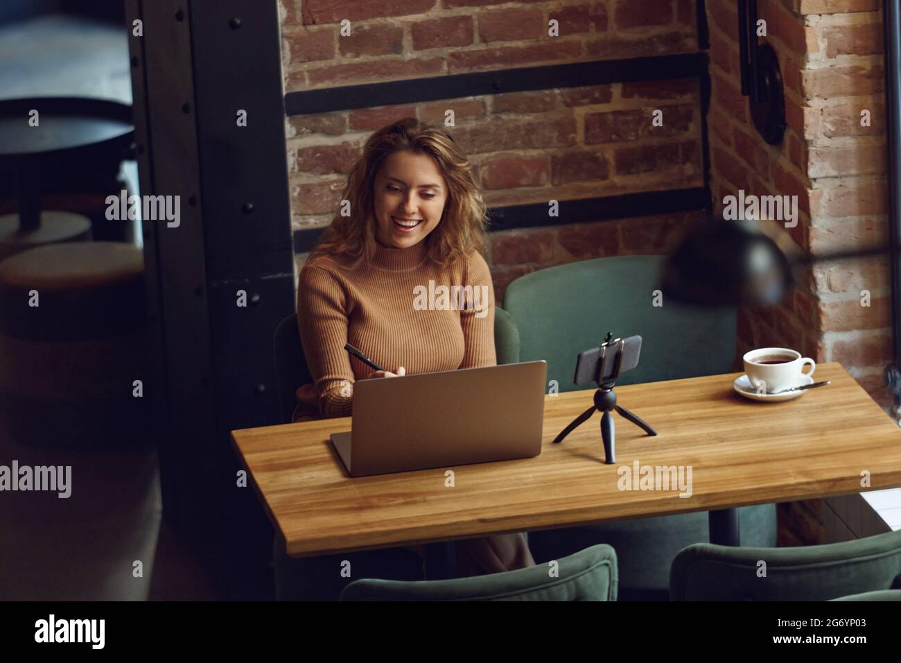 Femme souriante assise à table avec ordinateur portable et smartphone Banque D'Images
