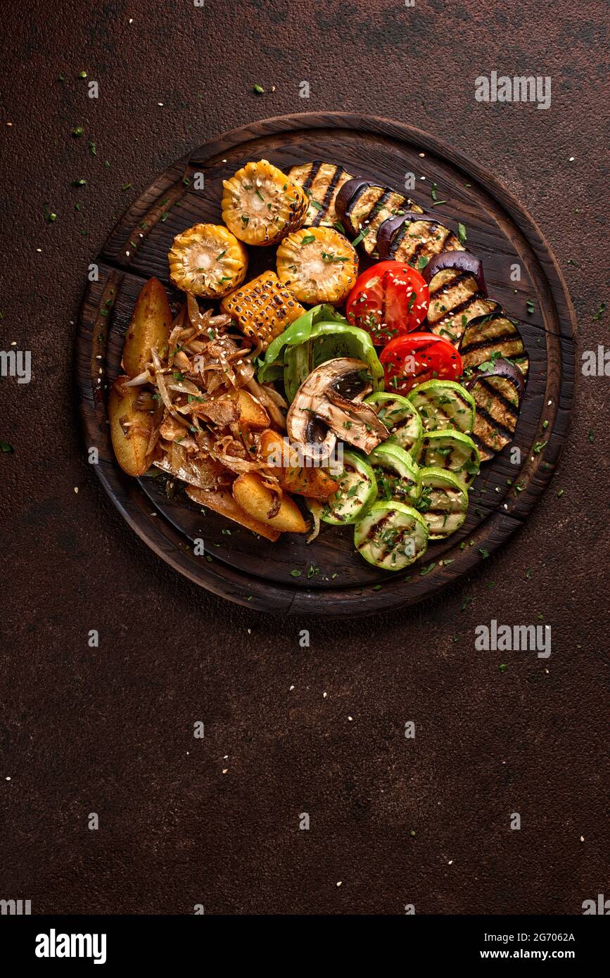 une grande portion de légumes et de champignons frits de couleur sur un plateau en bois sur fond sombre. Banque D'Images