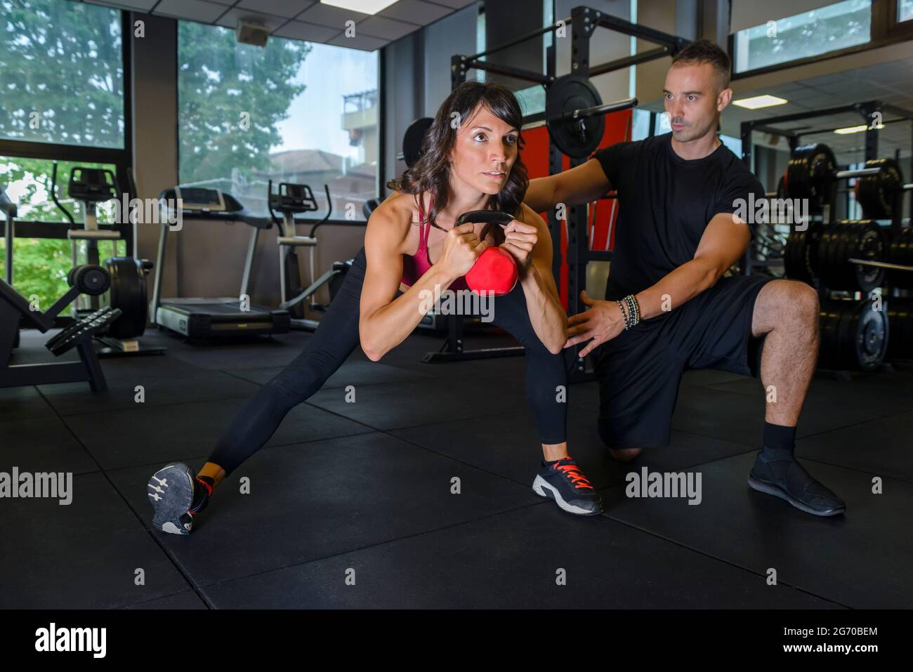 Gros plan d une jeune femme de fitness forte et concentree dans des vetements de sport qui fait des retouches sur les kettlebells a la salle de gym interieure pendant qu un entraineur personnel