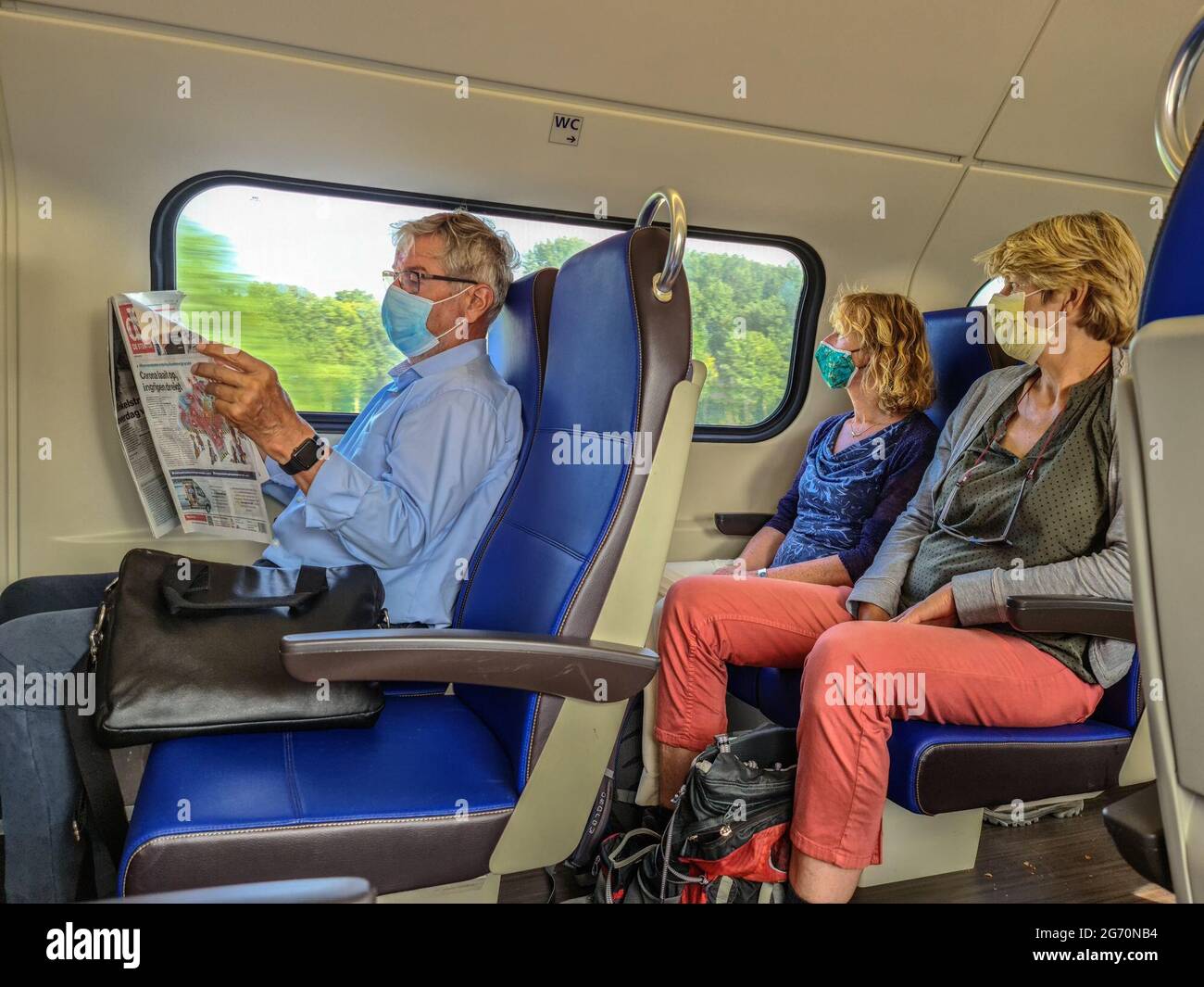 Amsterdam, pays-Bas. 9 juillet 2020. Passagers, deux femmes, un homme, dans le train portant un masque facial. L'homme est en train de lire un journal. En première page, la conférence de presse d'aujourd'hui est annoncée au cours de laquelle le Premier ministre Mark Rutte et le ministre de la Santé Hugo de Jonge ont annoncé plusieurs nouvelles restrictions concernant le coronavirus. Banque D'Images