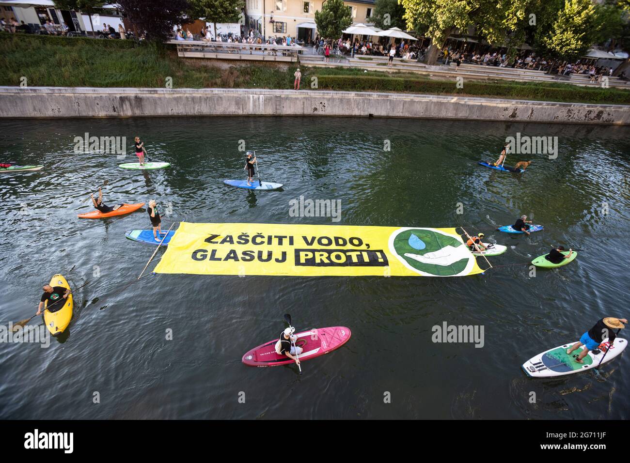 Ljubljana, Slovénie. 09e juillet 2021. Les manifestants sur des planches à pédales, des kayaks et des canoës sur la rivière Ljubljana tirent une grande bannière qui dit "protéger l'eau. Votez non ! » Pendant la manifestation, les manifestations antigouvernementales de vendredi contre les modifications proposées par le gouvernement à la loi sur l'eau ont continué d'encourager le public à voter contre la loi lors d'un référendum qui a lieu le 11 juillet. Crédit : SOPA Images Limited/Alamy Live News Banque D'Images