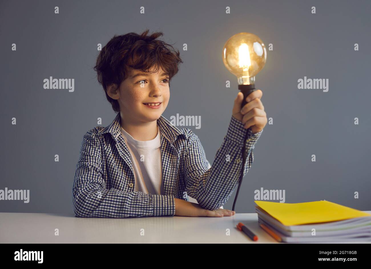 Un jeune garçon intelligent assis sur un bureau tenant une ampoule lumineuse portrait de studio Banque D'Images