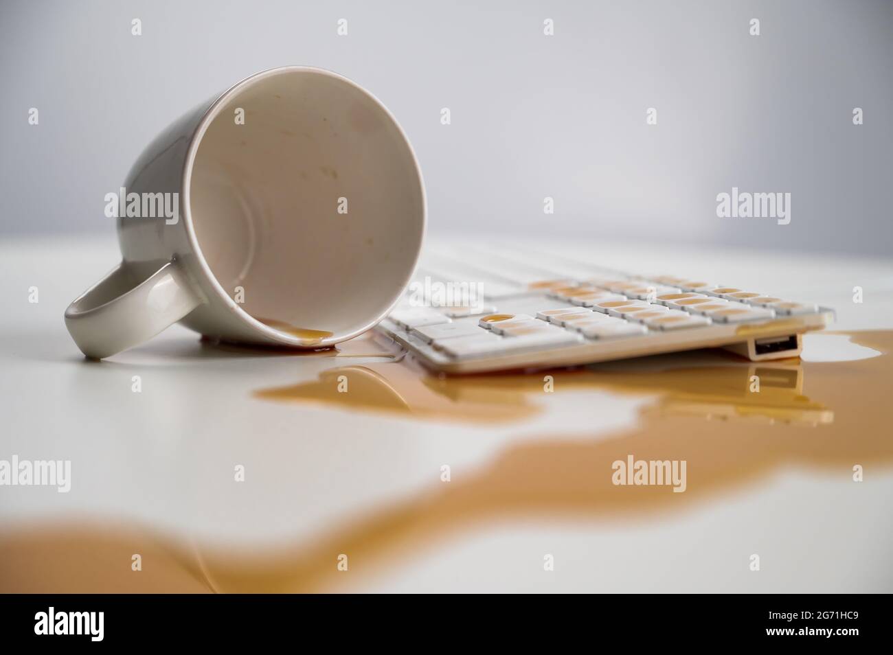 Tasse de café noir renversée sur le clavier de l'ordinateur sur la table blanche. Banque D'Images Tasse de café noir renversée sur le clavier de l'ordinateur sur la table blanche. Banque D'Images
