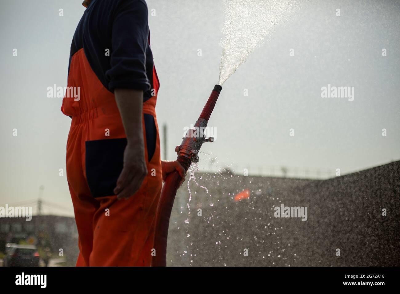 Un homme verse de l'eau dans un tuyau. Une fontaine d'eau d'une borne d'eau. Arrosage de la route. Banque D'Images
