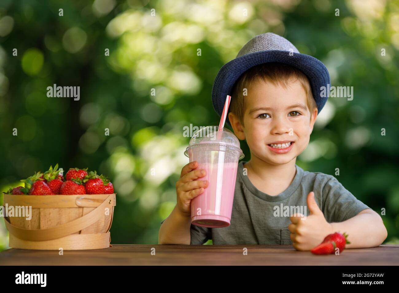 petit garçon tenant le verre plastique jetable de milkshake de fraise Banque D'Images