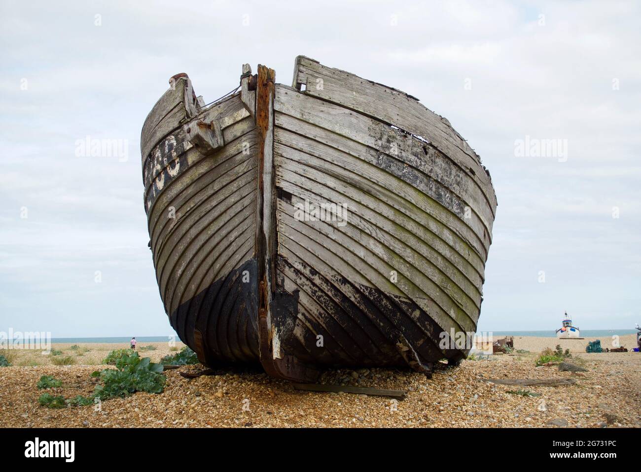 Dungeness, Angleterre, UK 09.2020 bateau abandonné sur une plage de galets dans le désert avec des plantes autour d'un ciel nuageux Banque D'Images