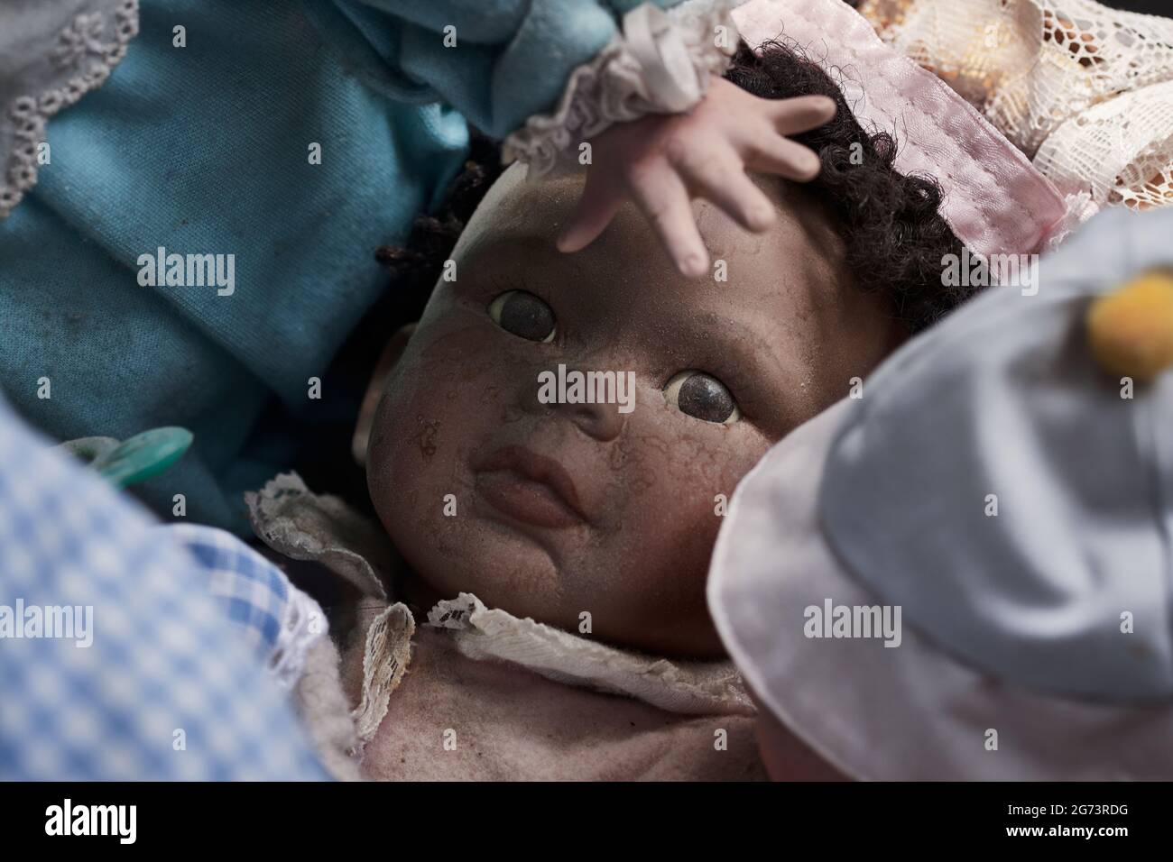 Visage d'un bébé poupée de peau sombre, sale et usé jouet vintage entouré d'autres poupées Banque D'Images
