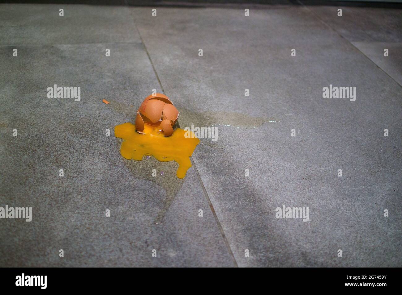 Œuf écrasé sur le sol carrelé gris avec coquille fissurée et cassée, jaune d'œuf et éclaboussures d'albumine Banque D'Images