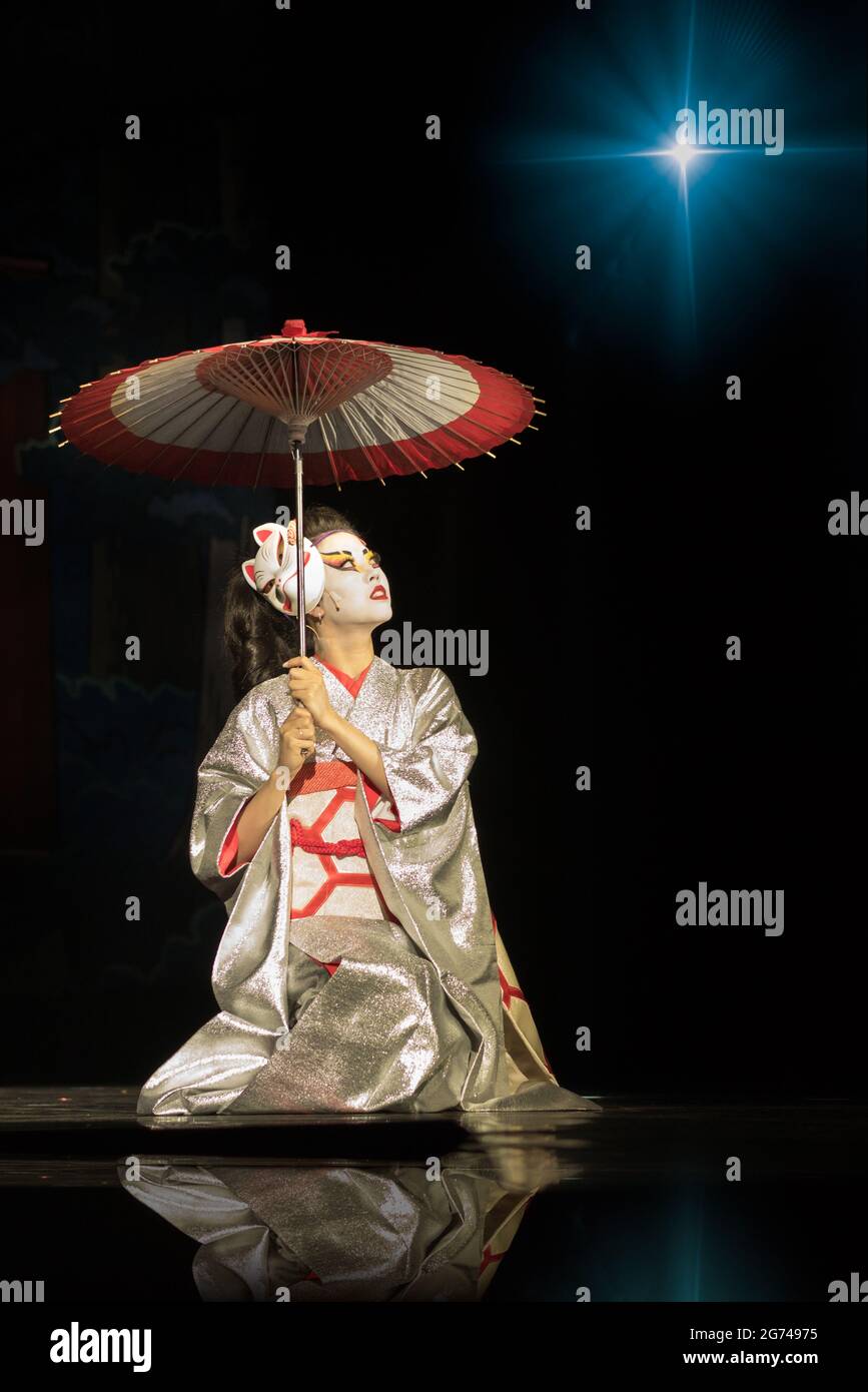 Geisha dans un kimono traditionnel avec parasol assis sur les genoux dans l'obscurité, Eclaircir par l'étoile et regarder vers le haut. Performances japonaises traditionnelles. Kin Banque D'Images