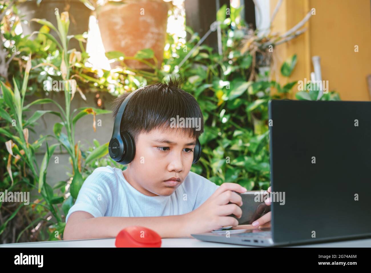 Un garçon asiatique portant un casque et une chemise blanche souriant et jouant à un jeu sur un smartphone. Banque D'Images Un garçon asiatique portant un casque et une chemise blanche souriant et jouant à un jeu sur un smartphone. Banque D'Images