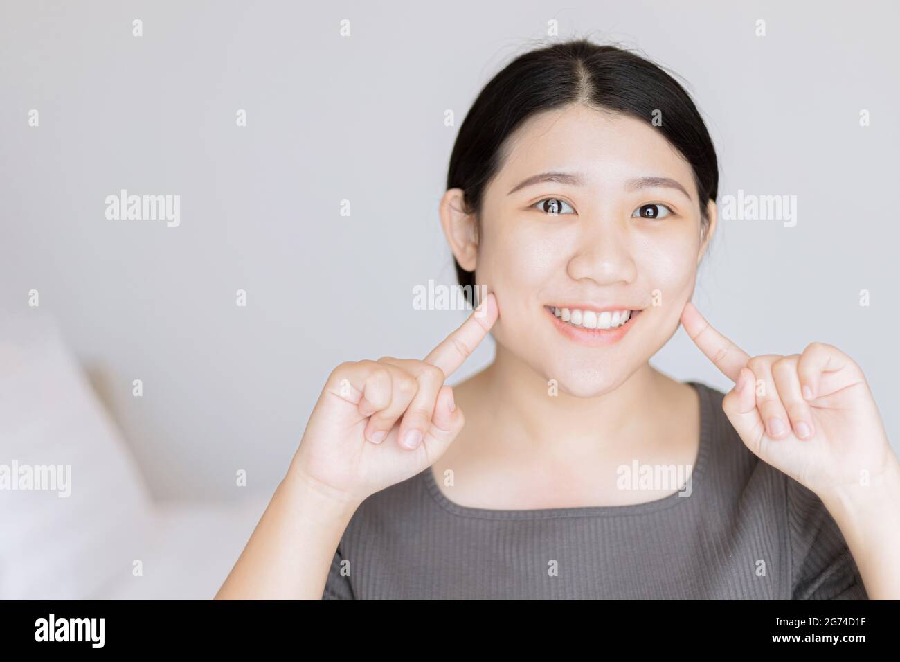 Belle jeune femme asiatique blanc bébé visage dents saines regarder le doigt point sur le visage pour le concept de soin de peau de visage. Banque D'Images