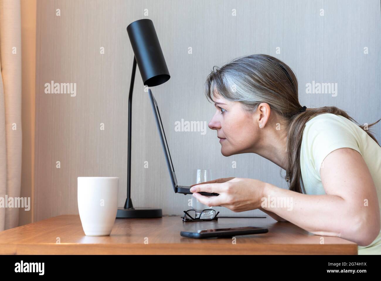 Femme avec une mauvaise vue travaillant dans son ordinateur portable, luttant pour voir Banque D'Images