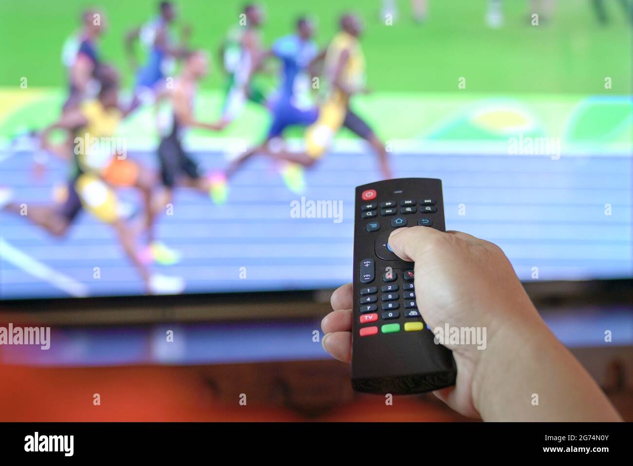 Homme regarde la piste et le terrain de sport à la télévision. Vue rapprochée de la télécommande. Banque D'Images