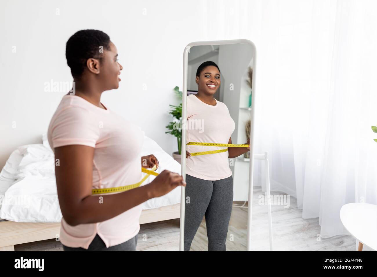 Femme noire en surpoids mesurant la taille avec du ruban près du miroir à  la maison, satisfaite du résultat amincissant, espace libre Photo Stock -  Alamy