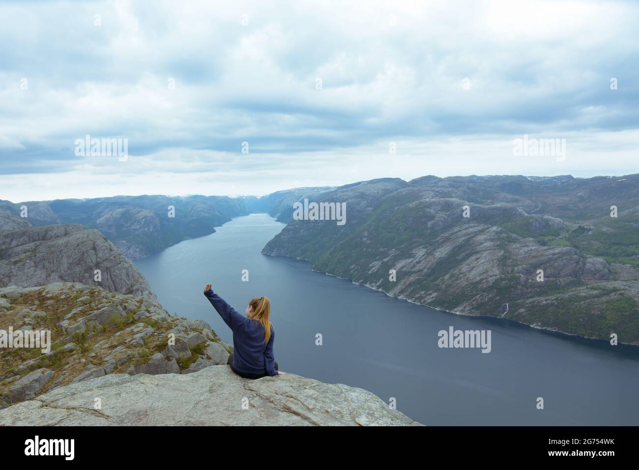 Une jeune femme caucasienne courageuse et aventureuse assise et posant sur le bord de la roche de Pulpit et agitant pendant qu'elle est photographiée. Banque D'Images