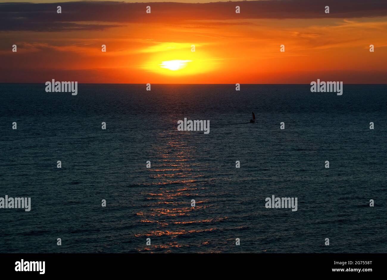 Petit voilier en mer au coucher du soleil. Banque D'Images