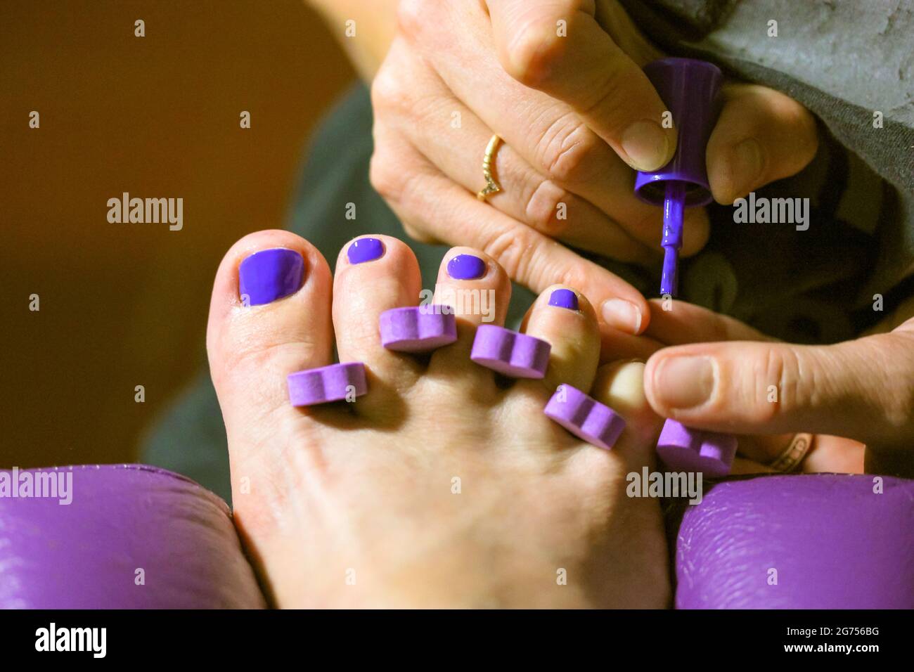 Le maître de pédicure applique du vernis à ongles violet vif aux ongles du client dans le salon de beauté. Doigts pour femmes, séparateur d'orteils de près. Accessoires de pédicure. Fille Banque D'Images