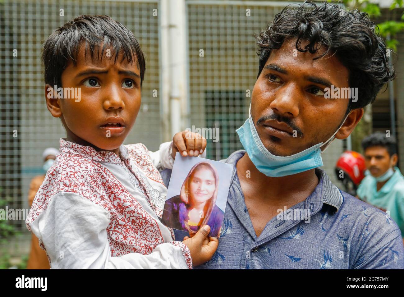 Un enfant tenant la photo de sa mère à l'hôpital du Dhaka Medical College pendant que les médecins collectent des échantillons de sang des parents des victimes o Banque D'Images