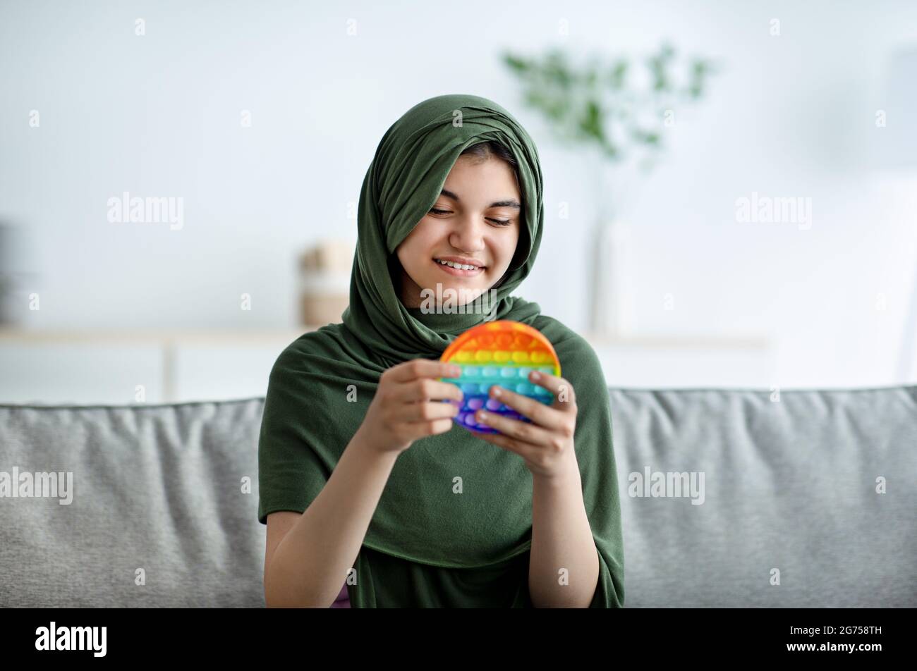 Joyeuse jeune fille musulmane dans hijab jouant avec POP IL antistress jouet à la maison Banque D'Images