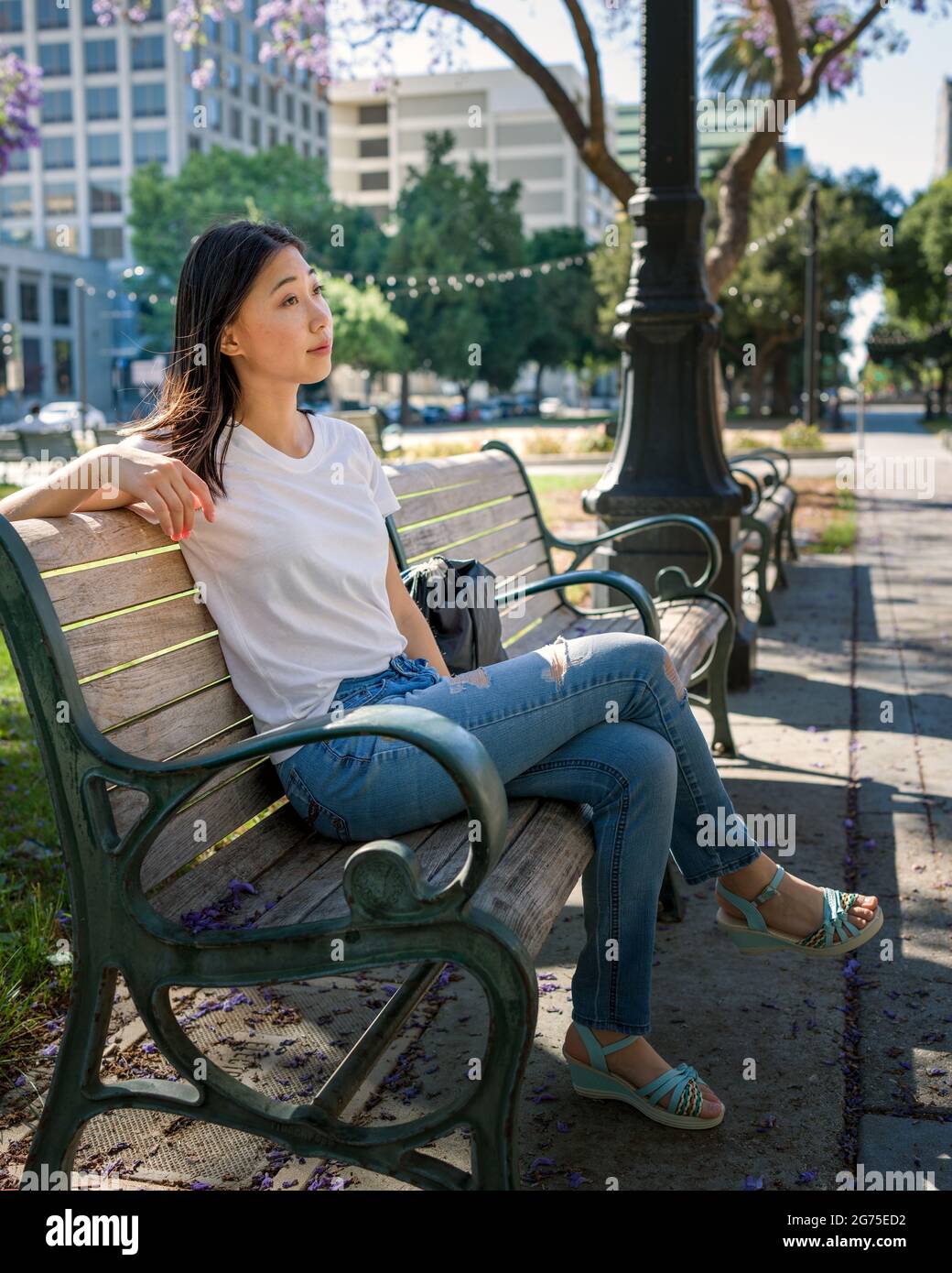 Jeune femme asiatique assise sur un banc de parc sous un arbre Jacaranda Banque D'Images