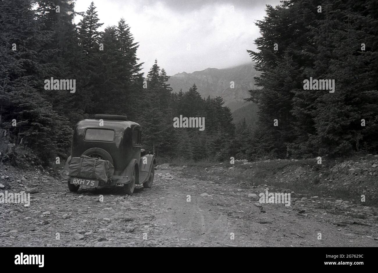 1935, historique, une voiture de l'époque, avec une plaque d'immatriculation britannique, bâillonez une piste rocheuse en gravier en haut d'une zone forestière des montagnes des Sudètes ou des Sudètes, Sudetenland, Tchécoslovaquie. Ils constituent la partie la plus haute de ce que l'on appelle le massif de Bohême, une série de chaînes de montagnes couvrant des parties de l'europe centrale. Banque D'Images