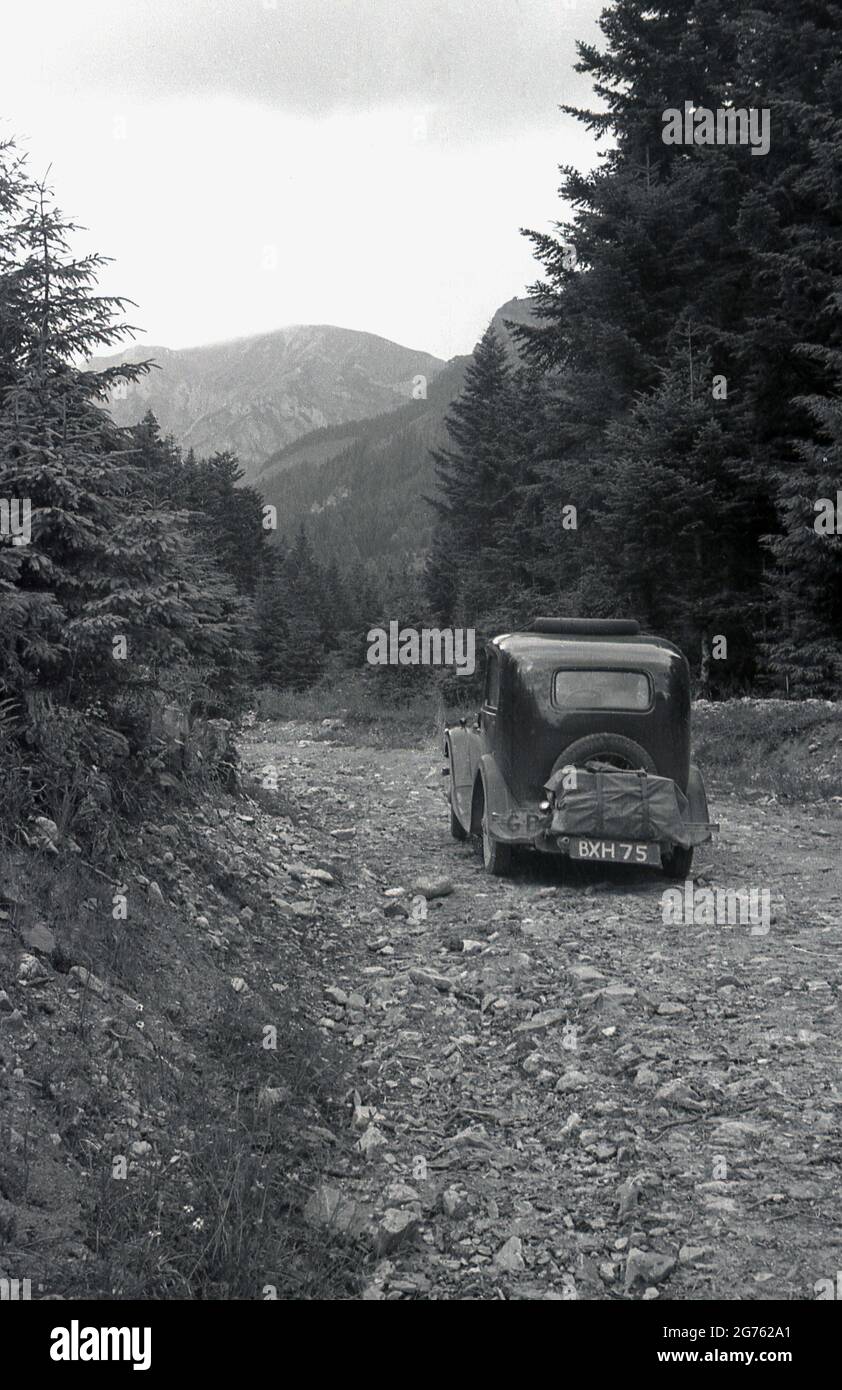 1935, historique, une voiture de l'époque, avec une plaque d'immatriculation britannique, bâillonez une piste rocheuse en gravier en haut d'une zone forestière des montagnes des Sudètes ou des Sudètes, Sudetenland, Tchécoslovaquie. Ils constituent la partie la plus haute de ce que l'on appelle le massif de Bohême, une série de chaînes de montagnes couvrant des parties de l'europe centrale. Banque D'Images