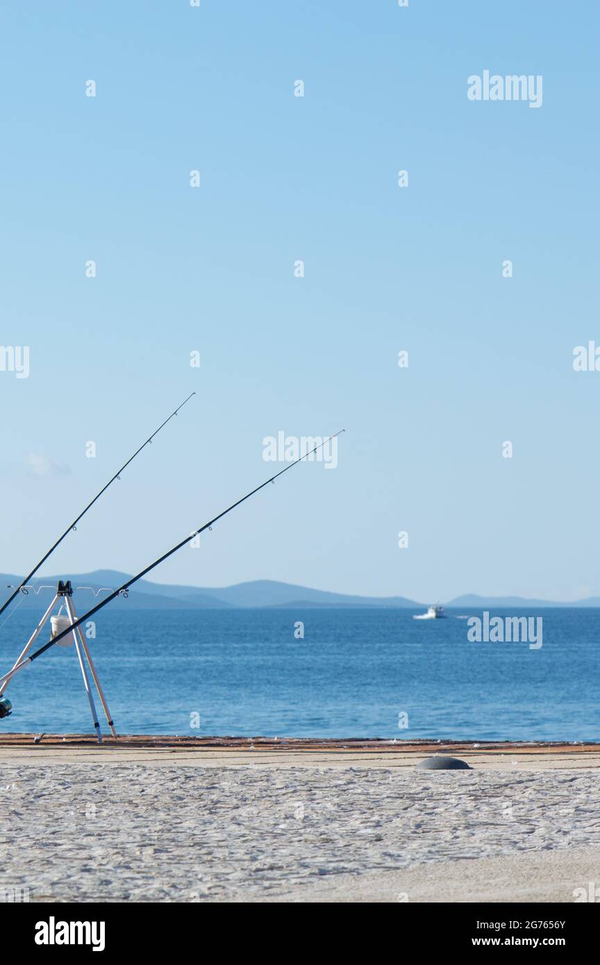 Des cannes à pêche sur le quai au bord de la mer, avec un bateau en arrière-plan, attendant un poisson à mordiquer, sur le quai de Zadar, Croatie Banque D'Images