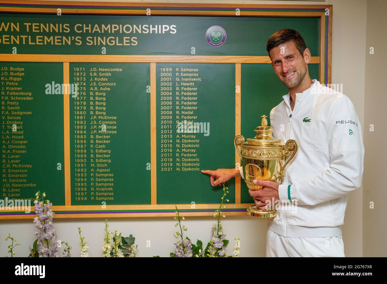 Novak Djokovic se présente avec le Trophée des célibataires de Gentlemen  devant le tableau des honneurs après la finale des célibataires pour hommes  le treize jour de Wimbledon au All England Lawn