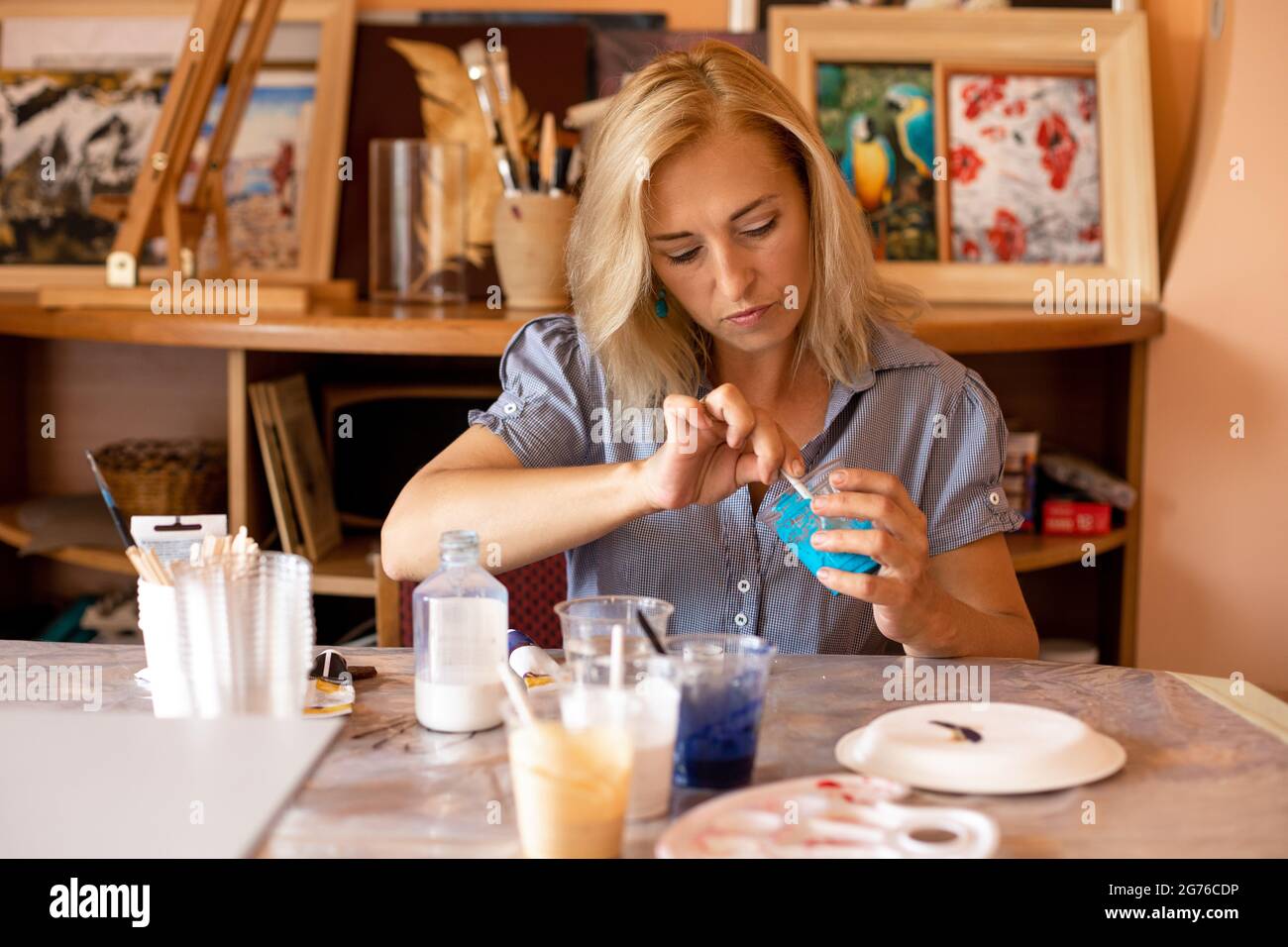 La femme se concentre sur mélanger la peinture turquoise avec la tasse et se prépare au travail. Travaillez dans un atelier de création. Peintures d'intérieur. Design et inspiration Banque D'Images
