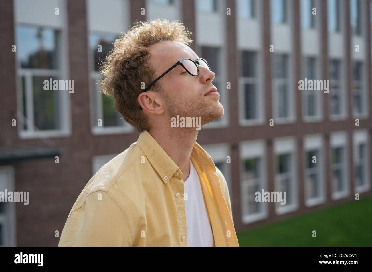 Jeune homme pensif avec des yeux fermés respirant de l'air frais, se relaxant dans le parc. Concept de détox numérique Banque D'Images