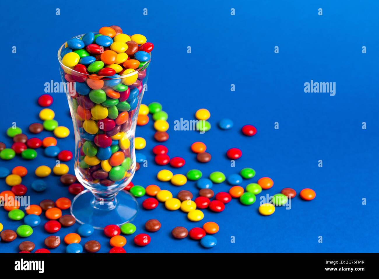 Un verre rempli de boutons de chocolat enrobés de bonbons de couleur arc-en-ciel Banque D'Images