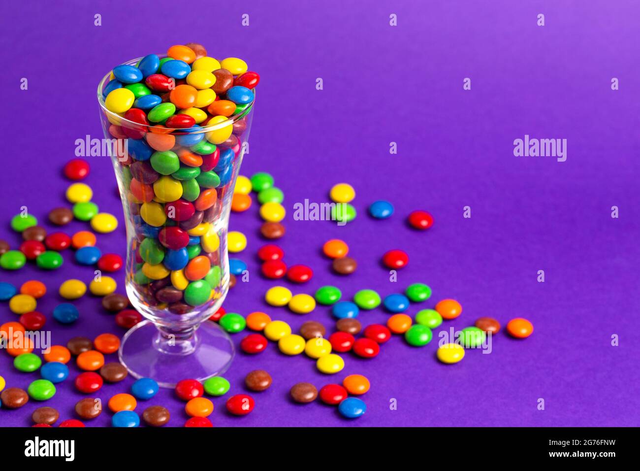 Un verre rempli de boutons de chocolat enrobés de bonbons de couleur arc-en-ciel Banque D'Images