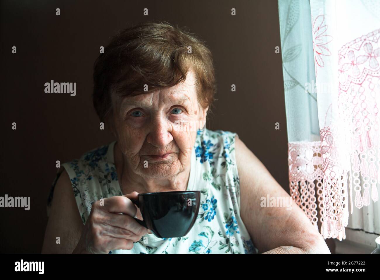 Portrait d'une vieille femme boit du thé à sa maison. Banque D'Images