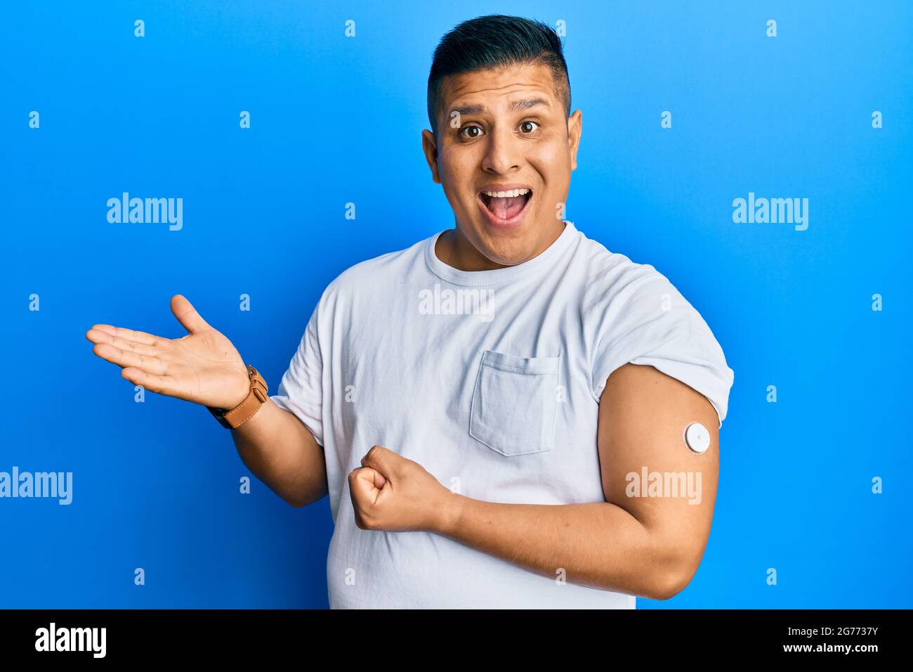 Jeune homme latin utilisant le bouton du glucomètre célébrant la réalisation avec le sourire heureux et l'expression du gagnant avec la main levée Banque D'Images