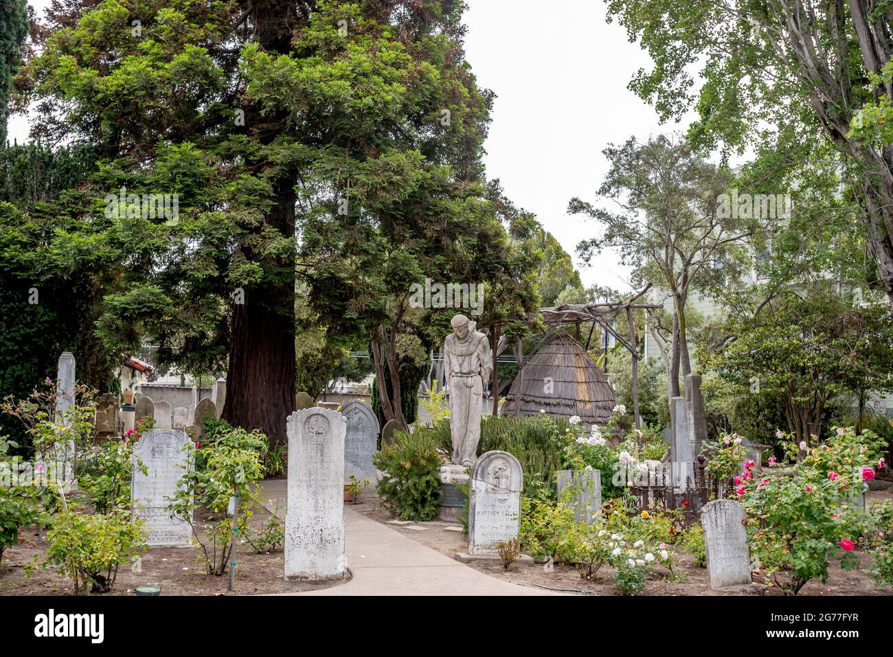 Cimetière de l'église San Francisco Mission Dolores. Une statue du Père Junipero Serra contraste avec une hutte familiale indigène de style Ohlone. Banque D'Images