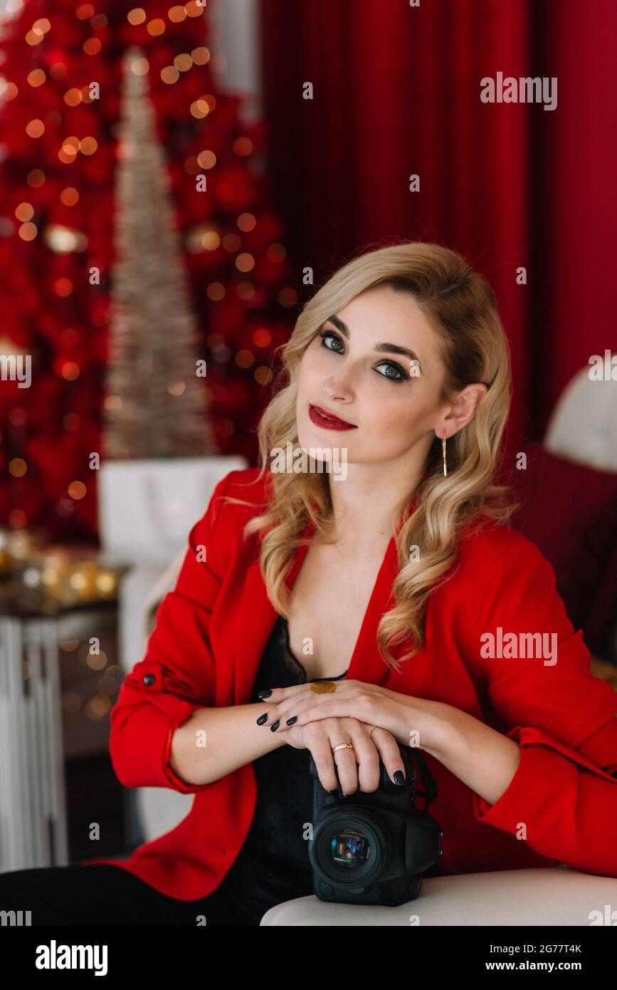 Belle femme photographe en rouge avec un appareil photo dans ses mains contre le fond des lumières bokeh d'un arbre de Noël. Bonne année 2021. Soft s Banque D'Images