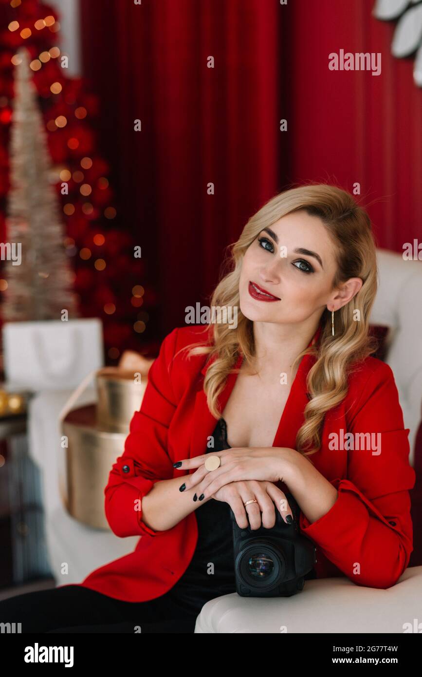 Belle femme photographe en rouge avec un appareil photo dans ses mains contre le fond des lumières bokeh d'un arbre de Noël. Bonne année 2021. Soft s Banque D'Images